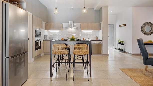 A modern kitchen with a central island, two bar stools, and a dining area with a chair.