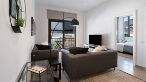 A modern living room with a sofa, a glass coffee table, a flat-screen TV, and a balcony with a view.