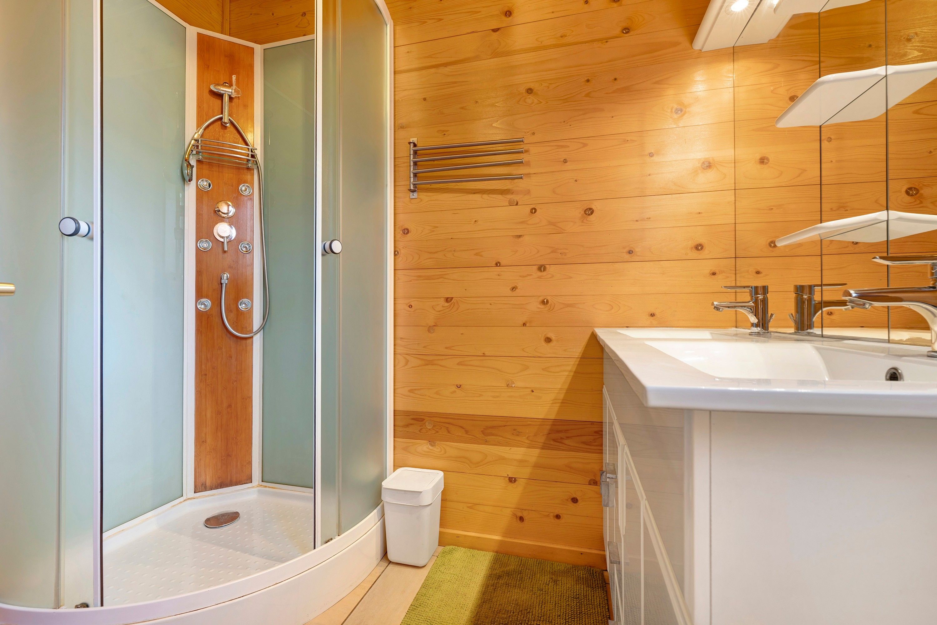Une salle de bain avec douche, lavabo et lambris en bois.