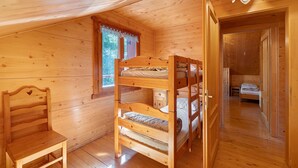 Une pièce de cabane en bois avec des lits superposés, une fenêtre et une porte donnant sur une autre pièce.