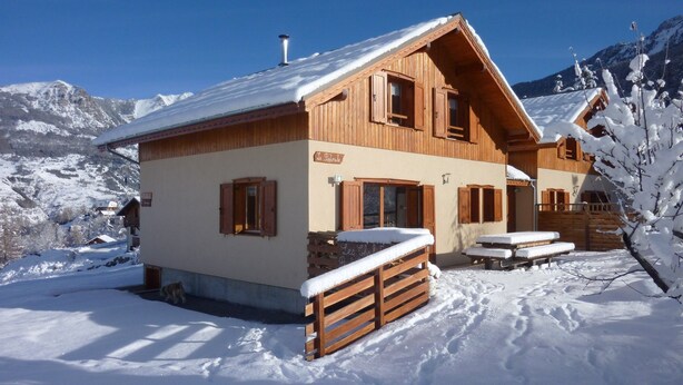 Un chalet en bois avec un toit à pente, des volets en bois et un sol recouvert de neige.