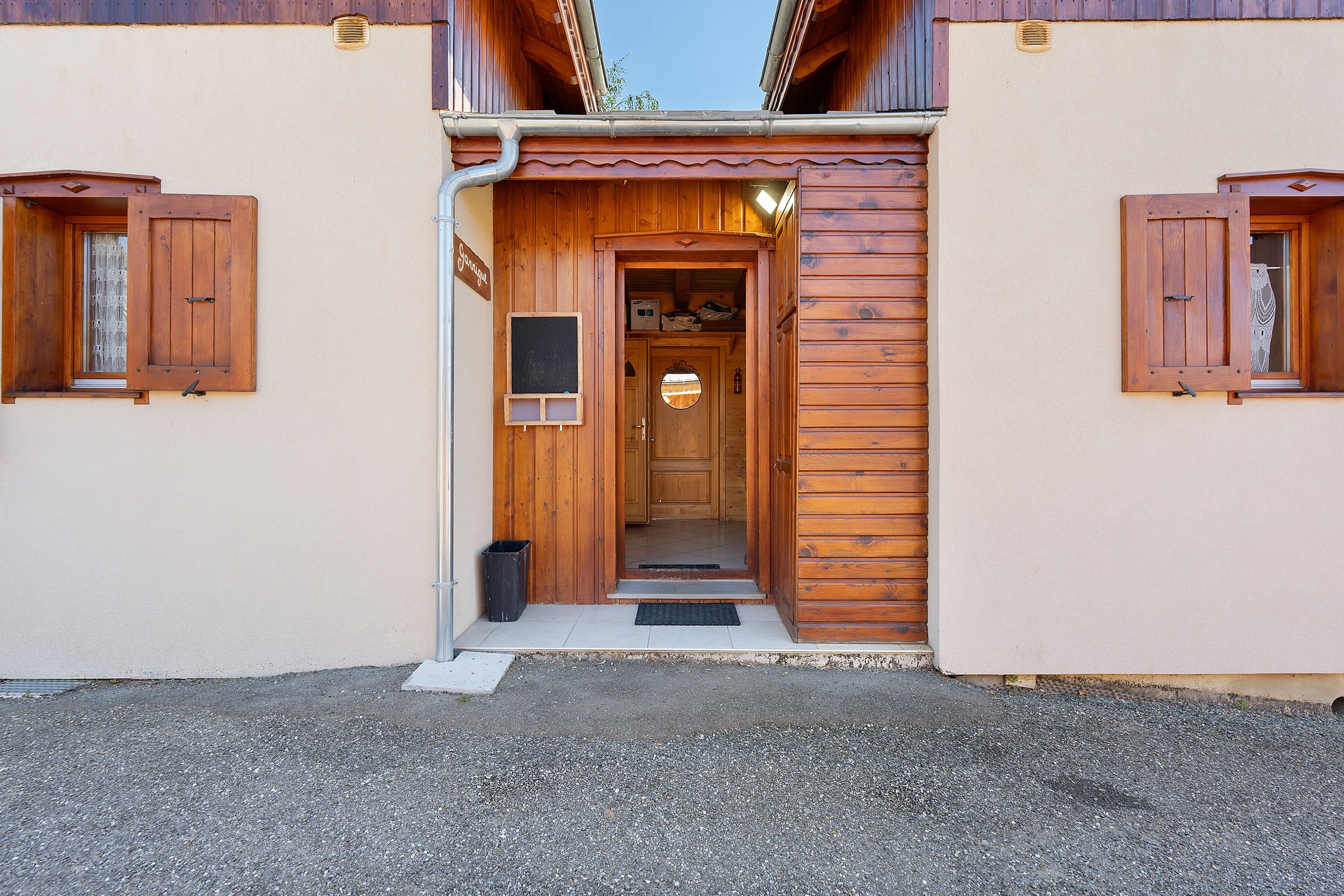 Une entrée en bois avec une porte, une petite fenêtre et une poubelle.