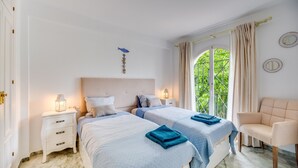 Un dormitorio con dos camas, una mesita de noche, una silla y una ventana con cortinas.