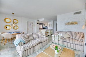 A modern living room with striped sofas, a glass coffee table, and a dining area with a white table and chairs. - Apartment 'Estepona Beach' with Sea View, Wi-Fi and Air Conditioning (estepona)
