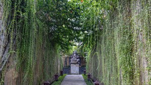 A pathway flanked by lush greenery and a statue, leading to a stone structure. - Wana Bucu Villas by GenuineHost (Ubud)