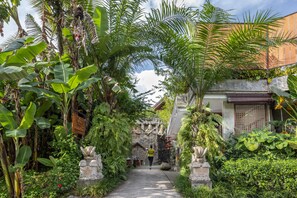 A pathway flanked by lush greenery and stone statues, leading to a traditional building with a tiled roof. - Wana Bucu Villas by GenuineHost (Ubud)
