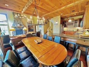 A spacious dining area with a large wooden table and blue chairs, a stone fireplace, and a kitchen in the background. - Stunning Treetop Condo in Stratton, VT with brand new Hot Tub (Stratton)