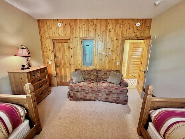 Una habitación acogedora con un panel de pared de madera, un sofá, un aparador de madera y una cama.