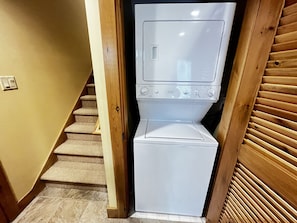 Un lavadero con lavadora y secadora, una puerta de madera y una escalera con alfombra.