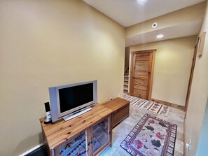 Una sala de estar con televisor de pantalla plana sobre un soporte de madera, un mueble bajo y un tapete estampado.