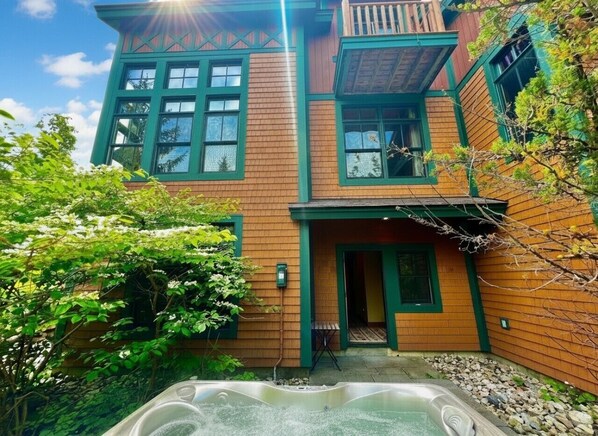 A two-story building with a hot tub in the foreground, surrounded by greenery. - Stunning Treetop Condo in Stratton, VT with brand new Hot Tub (Stratton)