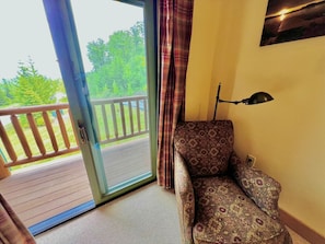 Una habitación con un sofá estampado, una lámpara y vistas a un balcón con barandilla.