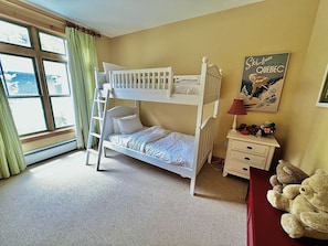 A bunk bed room with a ladder, a small bedside table with a lamp, and a poster on the wall.
