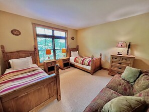 A bedroom with two wooden beds, a wooden nightstand, a wooden dresser, and a window with blinds.