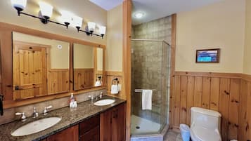 Een badkamer met houten lambrisering, een dubbele wastafel, een douchecabine van glas en een toilet.