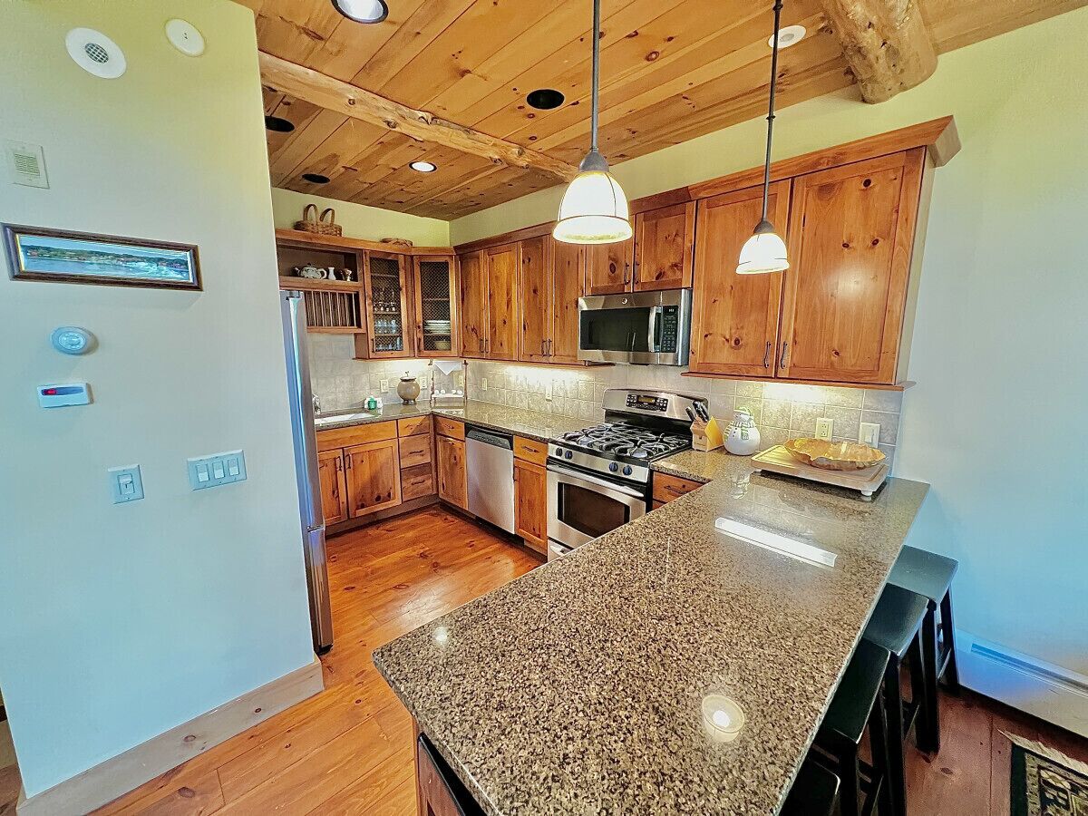 A kitchen with wooden cabinets, granite countertops, stainless steel appliances, and pendant lighting.