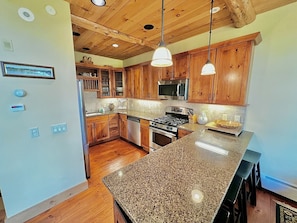 Una cocina con gabinetes de madera, encimeras de granito, estufa de acero inoxidable e iluminación colgante.