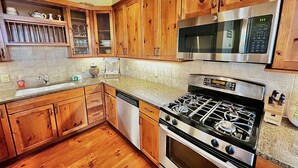 Una cocina con armarios de madera, estufa de acero inoxidable, microondas y lavavajillas.