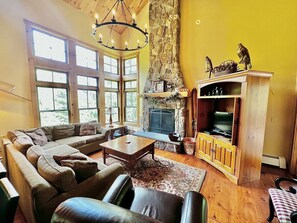 Una sala de estar acogedora con chimenea de piedra, ventanas amplias y un mueble de madera para entretenimiento.