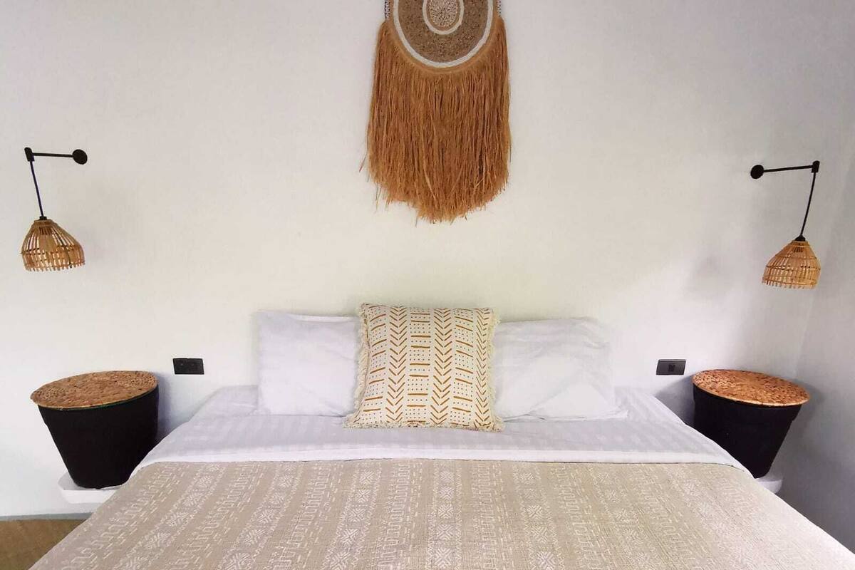 Quarto com uma cama grande, duas mesas de cabeceira, um adorno pendurado na parede e duas luminárias fixadas na parede.