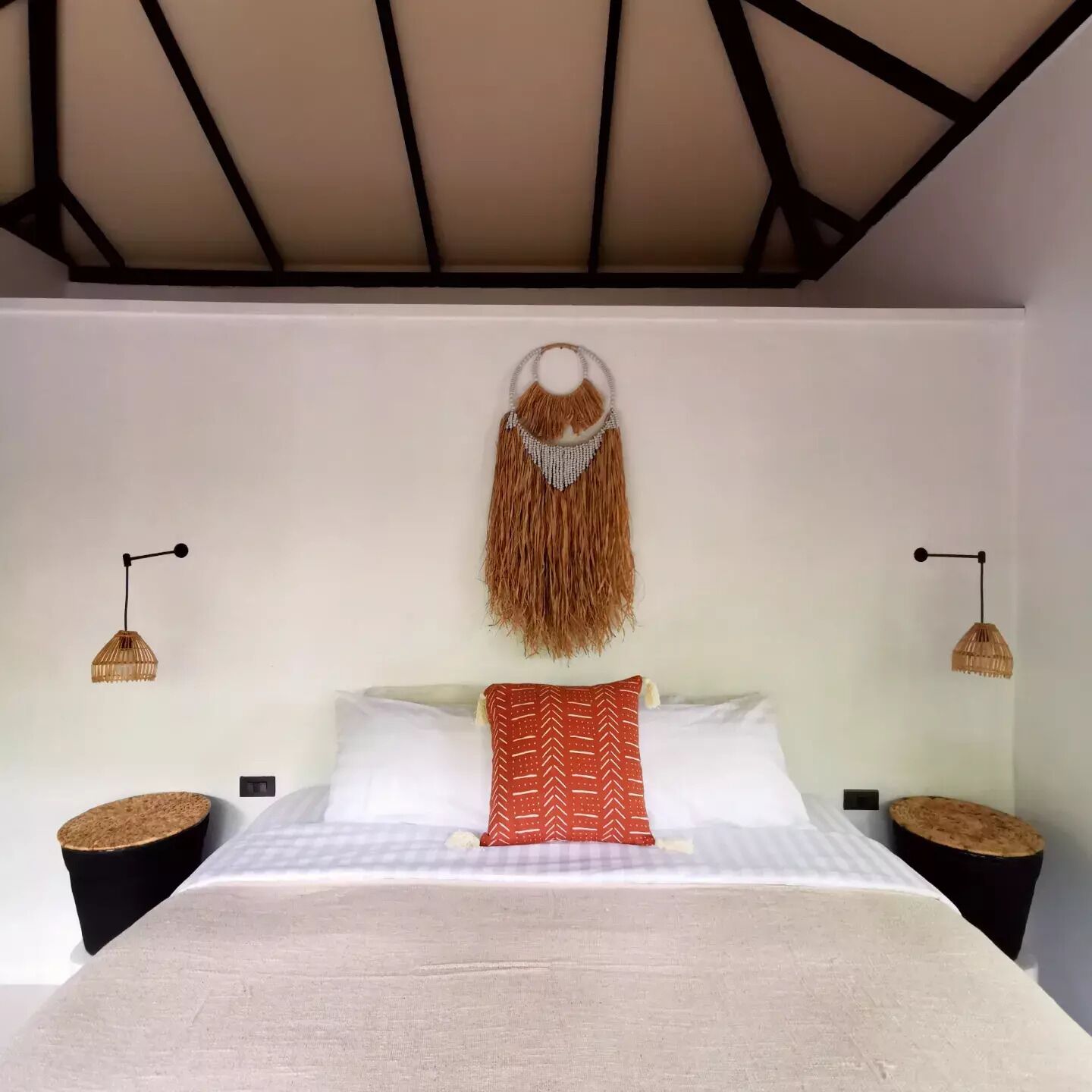 A bedroom with a bed, two bedside tables, a hanging macrame wall decoration, and two wall-mounted lamps.