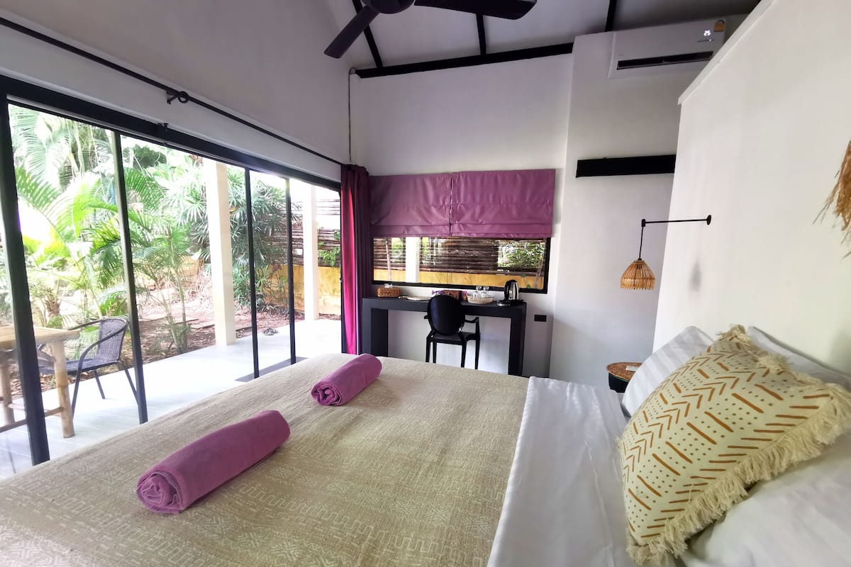 Quarto de hotel moderno com uma cama grande, uma escrivaninha e vista para um jardim.
