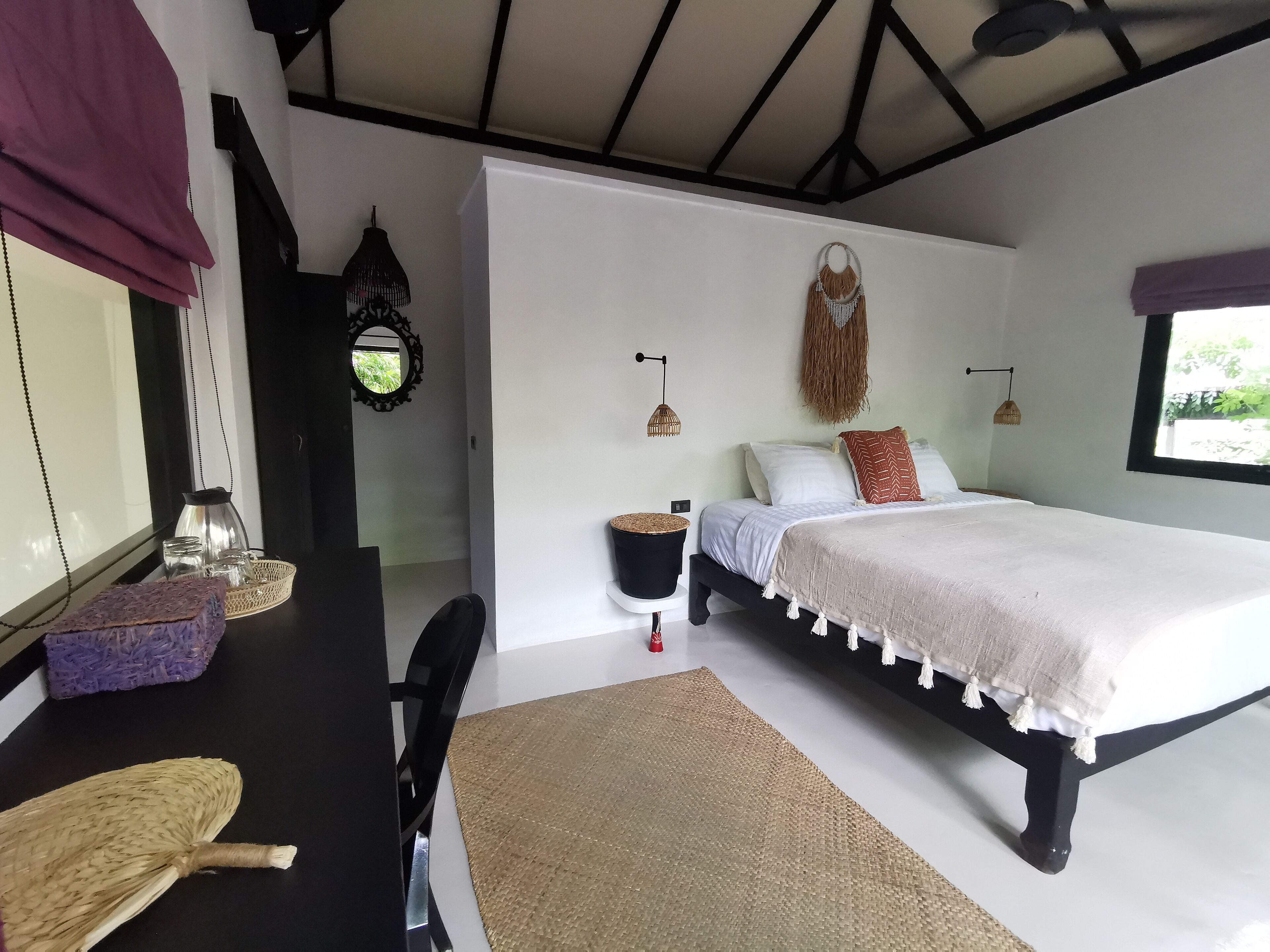 A bedroom with a bed, a desk, a chair, a window, and a ceiling fan.