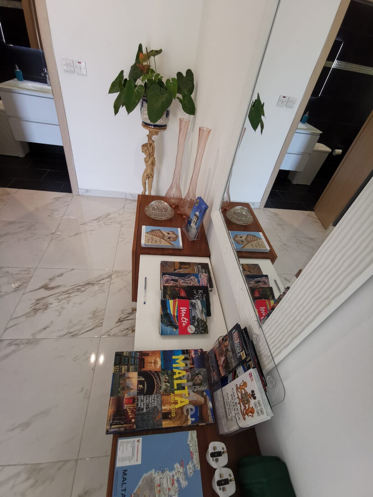 A room with a marble floor, a table with magazines, a plant, and a radiator.