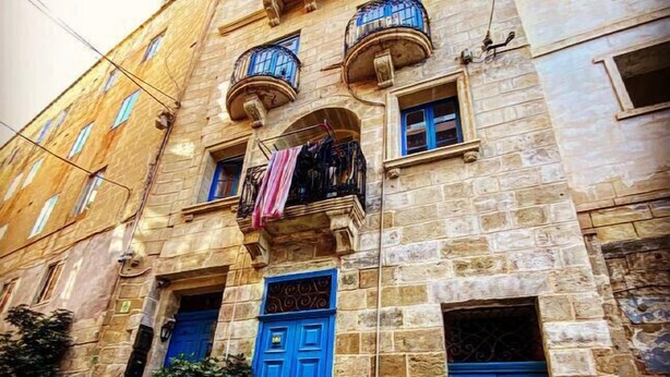 Un edifici de pedra amb portes i finestres blaves, un balcó amb roba i plantes en testos.