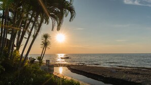 Uma praia com palmeiras, um barco e um pôr do sol.