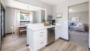 Une cuisine moderne avec des meubles blancs, un lave-vaisselle encastré et un coin repas comprenant une table et des chaises en bois.
