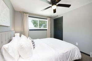 Een slaapkamer met een bed, een plafondventilator, een raam met gordijnen en een deur.