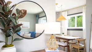 Un salon moderne avec un miroir rond, une plante en pot, une table basse en bois, un livre, une table à manger avec des chaises et une lampe suspendue.