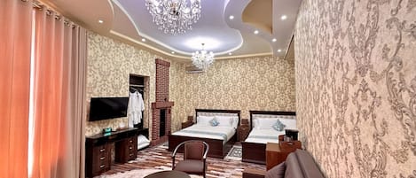 Una habitación de hotel con una cama grande, un sofá, un televisor, una araña y papel tapiz estampado.