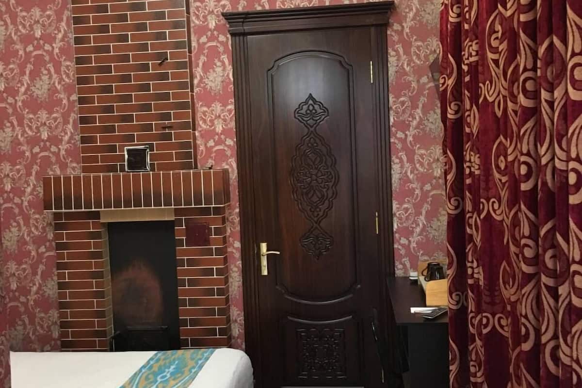 A bedroom with a brick fireplace, a large wooden door with intricate carvings, and a bed with a patterned bedspread.