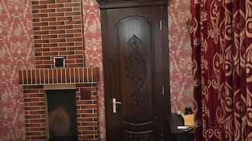 A bedroom with a brick fireplace, a large wooden door with intricate carvings, and a bed with a patterned bedspread.
