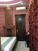 Un dormitorio con chimenea de ladrillo, una puerta grande de madera con intrincados grabados y una cama con colcha estampada.