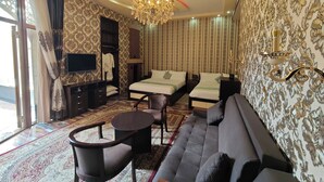 Une chambre d’hôtel avec deux lits, un canapé, une télévision, un lustre et un papier peint à motifs.