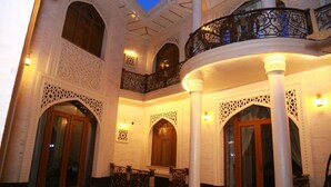 Un intérieur richement décoré, avec des portes en arc de cercle et des motifs blancs complexes, un balcon orné de balustrades en fer forgé et une colonne centrale.