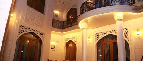 An ornate interior with arched doorways and intricate white detailing, a balcony with wrought iron railings, and a central column.