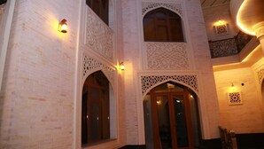 Un bâtiment dont la façade est ornée de motifs complexes en briques blanches, et qui présente des portes et des fenêtres en bois richement décorées.