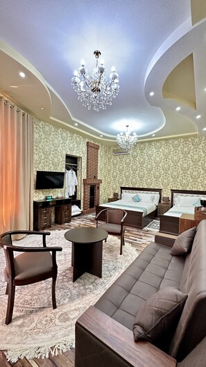 A spacious living room with a large sofa, armchairs, a coffee table, and a TV. There is a fireplace, a chandelier, and patterned wallpaper. - Mosaic Boutique Hotel (Samarkand)