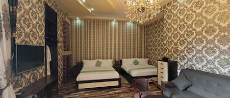 A hotel room with a large bed, a sofa, a TV, and a chandelier.