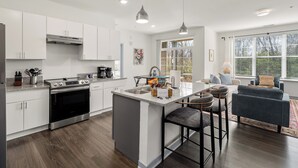 A modern kitchen with white cabinets, a central island, bar stools, and a dining area with a sofa and table. - Dublin 2BR | Pets welcome | Ground Floor | Views (Dublin)