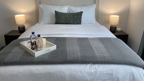 A neatly made bed with white and grey bedding, two bedside lamps, and a tray with toiletries. - The Queen of Dublin | Luxury 2BR Near Bridge Park | Pool + Gym (Dublin)