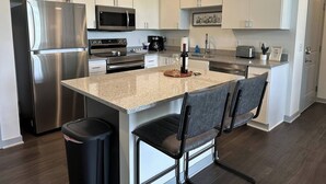 A modern kitchen with stainless steel appliances, a granite countertop, and a central island with bar stools. - Dublin 1BR | Pets OK | King bed | 0 stairs (Dublin)