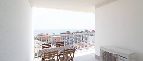 Un balcón con mesa y sillas, con vista a un paisaje urbano que incluye edificios y el mar.