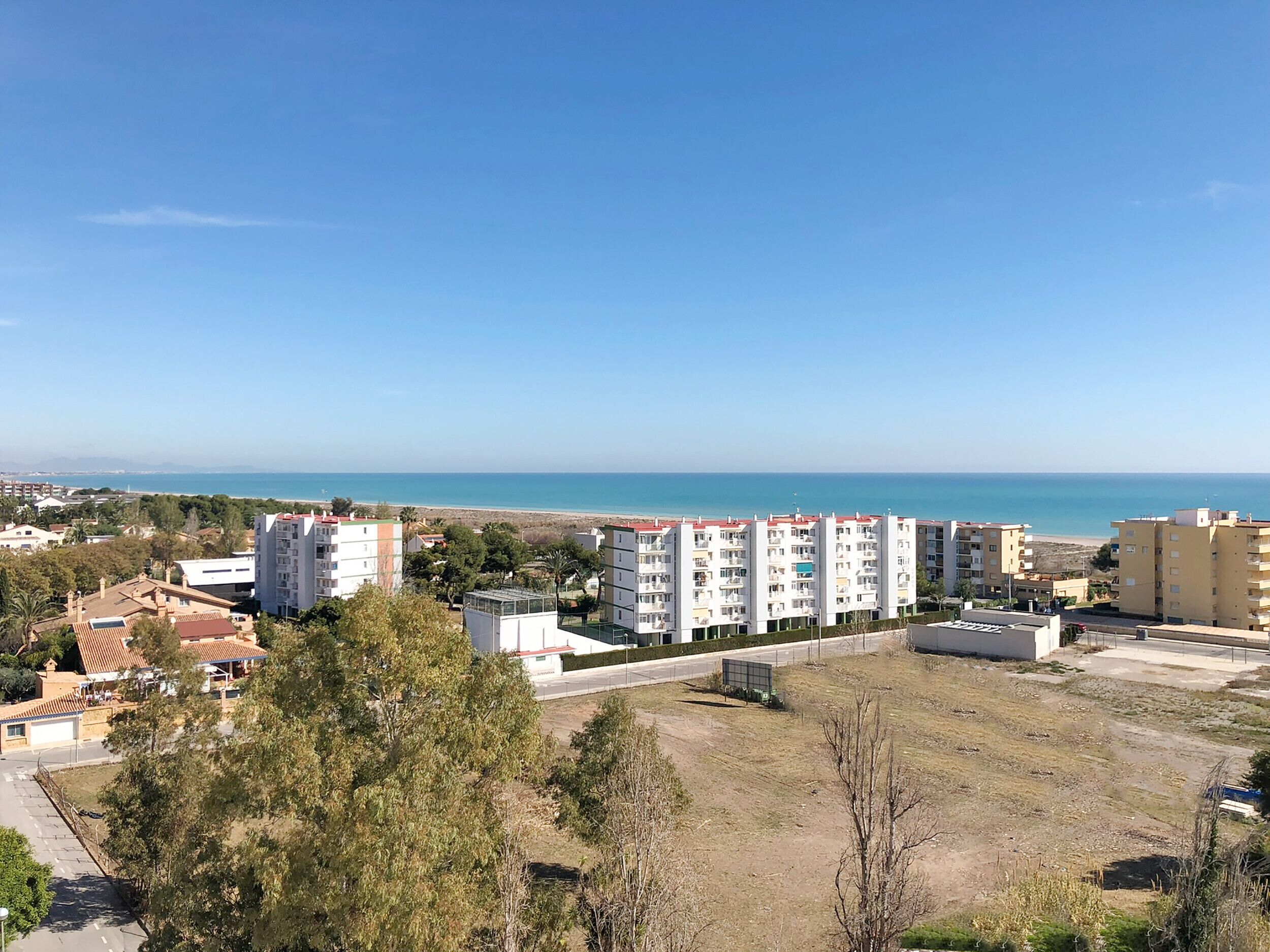 Un área residencial costera con edificios de varios pisos, cielo despejado y una playa al fondo.