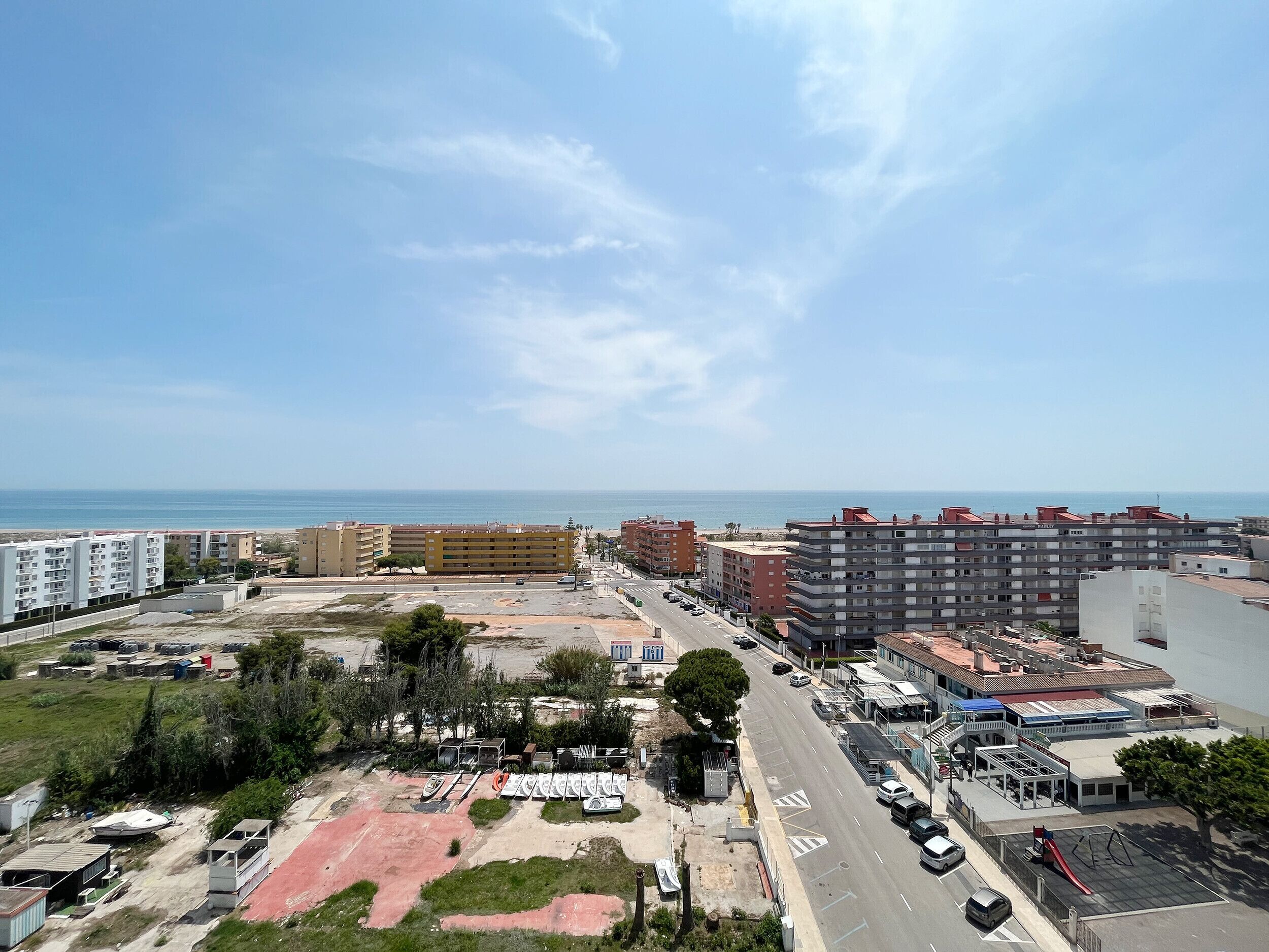 A coastal urban area with multi-story residential buildings, a parking lot, and a beach in the background.