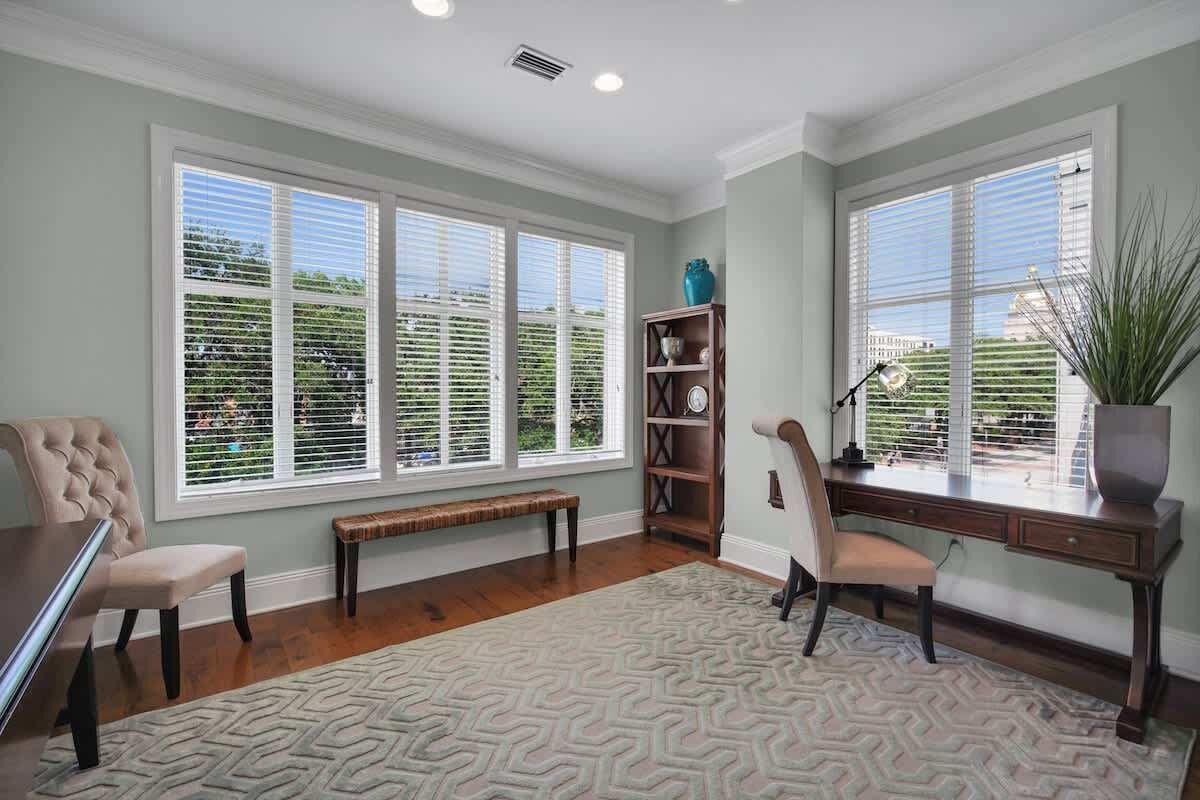 A room with large windows, a desk, a chair, a bench, and a bookshelf.